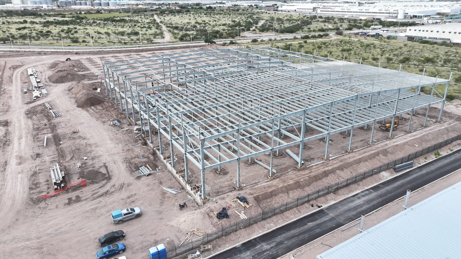 Montaje de estructura metálica junto a una nave en operación con paneles solares